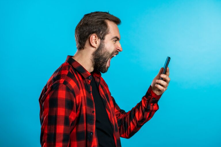 Angry modern hipster in red plaid shirt screaming down his mobile phone. Stressed and depressed man